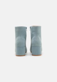 Bottines bleu clair avec un tissu texturé, talons carrés et fermetures éclair sur les côtés. Fini lisse avec un léger éclat et une semelle robuste.