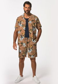 Conjunto de camiseta de manga corta y pantalones cortos en marrón con estampado floral tropical. Fabricado con tejido ligero, presenta un corte relajado y dos bolsillos.
