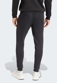 Μαύρο παντελόνι φόρμας με ελαφρώς στενή εφαρμογή, κατασκευασμένο από μαλακό ύφασμα. Διαθέτει ελαστικά τελειώματα στα μπατζάκια και πλαϊνές τσέπες· φορεμένο με λευκά αθλητικά παπούτσια.