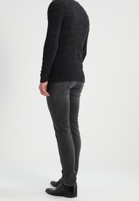 Svart stickad tröja med texturmönster, i kombination med slim-fit mörkgrå jeans. Svarta skinnskor avslutar outfiten. Bakifrån vy av kläder.