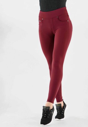 Leggings bordeaux a vita alta realizzati in un tessuto elastico, dotati di tasche frontali e accentuati da dettagli in metallo argentato. Abbinati a sneakers nere.