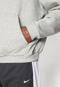 Grå sweatshirt med ribbede manchetter, med en sidelomme. Kombineret med mørkegrå sportsbukser, pyntet med et hvidt Nike-logo.