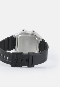 Bracelet de montre en caoutchouc noir avec un fond en acier inoxydable, au design angulaire argenté et avec une fermeture à boucle marquée.