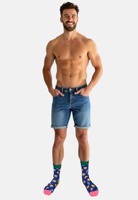 Denim shorts med opsmøgede kanter, lys blå farve. Farverige, mønstrede sokker med madvarer på en blå baggrund med pink og grønne accenter.