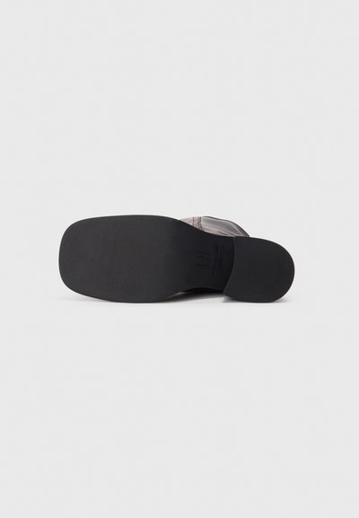 Chaussures noires avec une semelle en caoutchouc lisse, présentant un dessus gris texturé et des éléments de design minimalistes. Style plat sans matériel visible.