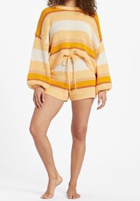 Gebreide oversized trui met oranje, witte en beige strepen; heeft een trekkoord in de taille en ballonmouwen; gecombineerd met bijpassende shorts.