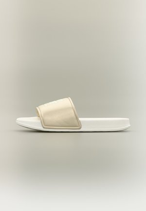 Beige og hvit skyvesandal med polstret tykk såle og bred stropp over foten, vist mot en enkel nøytral bakgrunn.