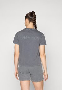 T-shirt en coton gris avec le logo "CHAMPION" dans une teinte légèrement plus foncée, associé à un short gris à rayures, présenté de dos.