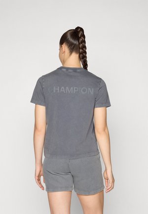 Šedé bavlnené tričko s logom "CHAMPION" v mierne tmavšom odtieni, v kombinácii so šedými pruhovanými šortkami, zobrazené zozadu.