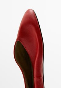 Red leather flat shoe with pointed toe and low sides showing brown inner lining, isolated on white background.