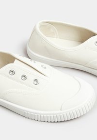 Scarpe slip-on bianche in tela con occhielli argentati, punta rotonda e suola in gomma con un motivo di grip testurizzato.