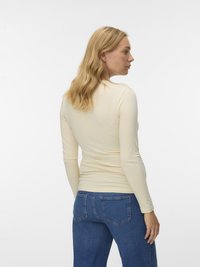 Pikad varrukad, hele kreemikas särk sileda kangaga, kombineeritud siniste teksapükstega, millel on tagataskud ja sirge lahendusega sääred.