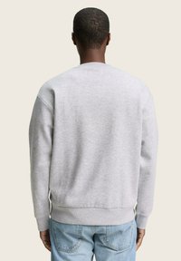 Pilkas megztinis su apvalia iškirpte, nertais rankogaliais ir apatine dalimi. Nėrinių mišinys su lygiu paviršiumi. Dėvimas su šviesiai mėlynomis džinsomis.