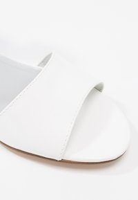 Sandales blanches en cuir lisse avec un design ouvert à l'avant. Elles présentent une large sangle au centre et une semelle plate.