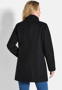 Cappotto nero con un tessuto testurizzato, colletto e maniche lunghe; arriva a metà coscia con un taglio dritto e dettagli di apertura sul retro.