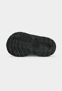 Μαύρη σόλα παπουτσιού Nike με διακοσμητικά σχέδια και κεντρικό λογότυπο Nike Swoosh, παρουσιασμένη σε λευκό φόντο.