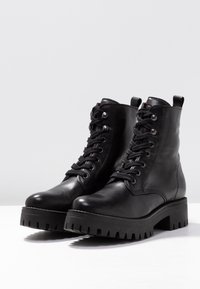 Černé kožené kotníkové boty s robustní podrážkou, kulatou špičkou a šněrováním v přední části. Obsahují poutko a kovové očko pro tkaničky.