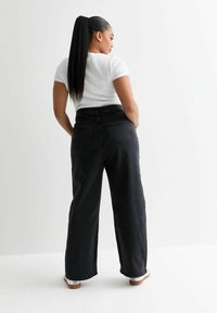 Breda svarta denimjeans med hög midja, utrustade med två bakfickor och en avslappnad passform. Kombinerat med en åtsittande vit ribbad t-shirt.