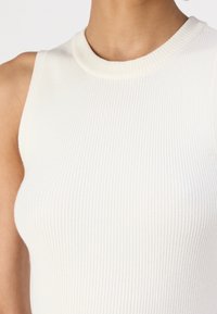 Valge, särgiservaga top, mis on valmistatud soonikust kangast ja millel on ümmargune kaelus. Omab pehmet tekstuuri ja keha lähedast siluetti.