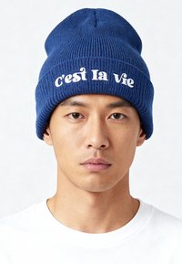 Bonnet côtelé bleu en matière tricotée, avec l'inscription « c'est la Vie » en texte cursif blanc sur le devant.