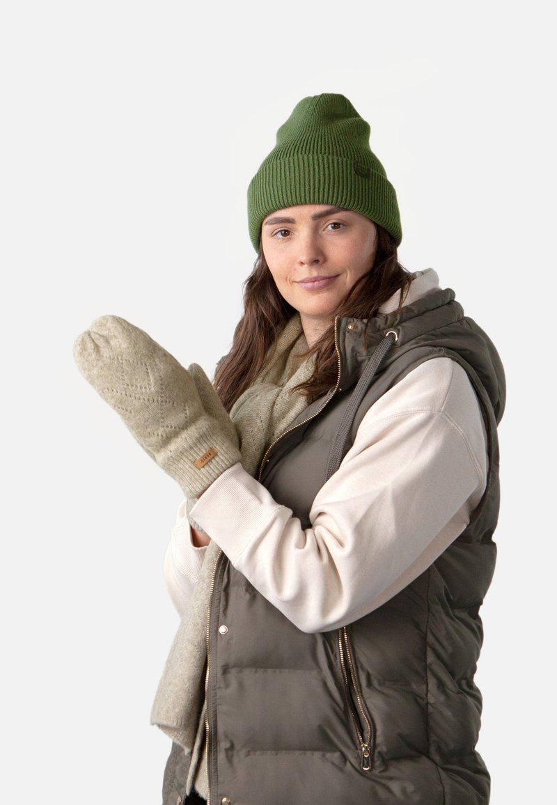 Moufles en tricot beige avec un motif texturé, bonnet vert clair, gilet matelassé gris sur un sweat crème, et écharpe claire.