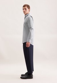 Camicia button-up azzurro chiaro con pattern e maniche lunghe, abbinata a pantaloni blu scuro e scarpe nere, vista di lato.