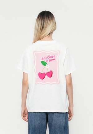 Hvit T-skjorte med rosa grafikk av kirsebærillustrasjoner og teksten "Som kirsebær i blomst" på ryggen, med en avslappet passform.