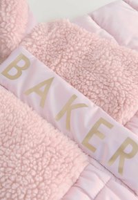 Rosa puffjacka med en plyschig, pälsliknande textur, med en blank panel märkta med "BAKER" i gyllene bokstäver på bröstområdet.