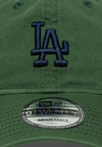 Πράσινο καπέλο με ρυθμιζόμενο λουράκι, διακοσμημένο με κεντημένο ναυτικό μπλε λογότυπο "LA". Περιλαμβάνει στρογγυλή αυτοκόλλητη ετικέτα New Era στο γείσο.