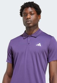 Lila Poloshirt mit einem Kragen-Design, kurzen Ärmeln und einem weißen Logo. Hergestellt aus glattem Stoff, hat es eine klassische Passform und eine Knopfleiste.