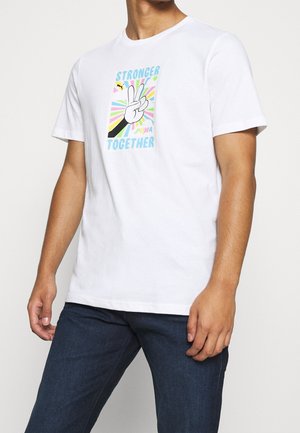 Camiseta de algodón blanca con un gráfico colorido que presenta un símbolo de paz, texto "MÁS FUERTES JUNTOS" y "PUMA", en un fondo con patrones en forma de rayo de sol.