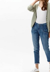 Cárdigan verde claro con botones, camiseta blanca sin mangas, jeans de mezclilla azul con bolsillos delanteros y zapatillas blancas. Diseño de atuendo casual presentado.