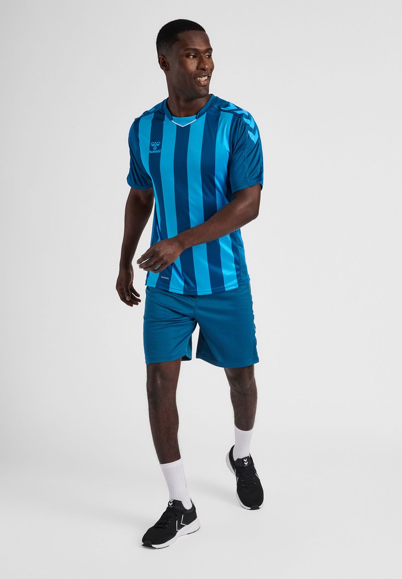 Blårandig idrottströja med korta ärmar, tillsammans med enfärgade blå shorts. Outfiten har fukttransporterande tyg och avslappnad passform.