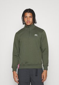 Felpa pullover verde oliva con colletto alto, zip a quarti e un piccolo logo bianco sul petto. Presenta polsini e orlo a coste.