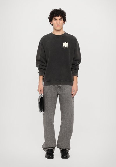 Mørkegrå hettegenser med hvit grafikk, avslappet passform og ribbede mansjetter, kombinert med brede grå jeans og svarte sko, holder en svart veske.