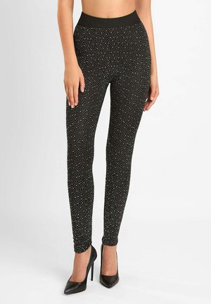 Czarne legginsy w kropeczki, miękka tkanina, wysoki stan i dopasowany krój, noszone z czarnymi wysokimi obcasami.