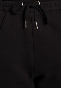 Pantalones deportivos negros con una tela texturizada, que cuentan con una cintura elástica y cordón con puntas metálicas. Diseño simple sin patrones.
