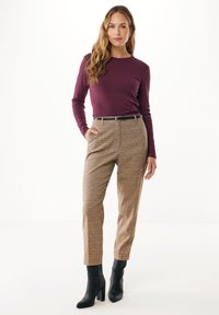 Maglietta a maniche lunghe color bordeaux abbinata a pantaloni a vita alta a quadri nei toni beige e marroni, completata da stivaletti neri alla caviglia.