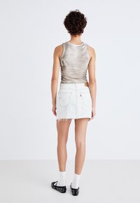 Szürke tank top, fehér farmer mini szoknya rojtos szegéllyel, és fekete slip-on cipők, strasszokkal. A modell háttal áll egy fehér háttér előtt.