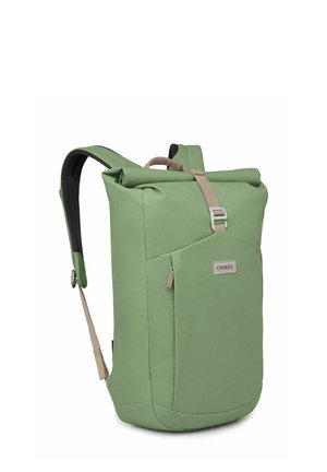 Sac à dos en tissu vert avec fermeture supérieure roulée, bretelles rembourrées et poche zippée à l'avant. Texture lisse et design minimaliste.