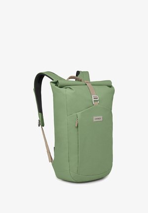 Sac à dos en tissu vert avec fermeture supérieure roulée, bretelles rembourrées et poche zippée à l'avant. Texture lisse et design minimaliste.