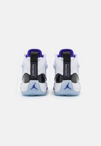 Bílé a černé tenisky s fialovými akcenty, s hladkým koženým svrškem, polstrovaným límcem a průhlednou modrou podrážkou.