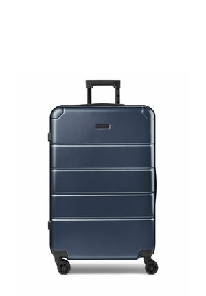 Valigia rigida blu navy con quattro ruote nere girevoli e manico estensibile nero in posizione verticale.