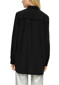Schwarzes Langarmhemd mit Kragen, das mit einem Yoke-Rücken und knöpfbaren Manschetten versehen ist. Kombiniert mit metallic-silbernen Hosen.