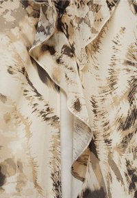 Blouse fluide avec un col à volants, présentant un motif abstrait beige et marron. Tissu doux et léger avec une texture lisse.