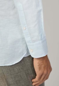 Camicia a maniche lunghe a righe blu chiaro e bianche con polsini abbottonati, realizzata in un tessuto liscio con una sottile texture.