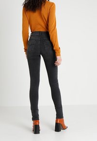 Jeans skinny de tiro alto negros, fabricados en denim, contrastados con una blusa larga naranja de textura. Tacones naranjas con un tacón grueso.