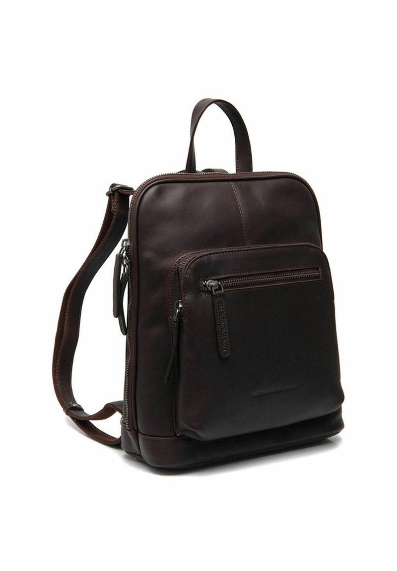 Un sac à dos en cuir marron foncé avec une poche zippée à l'avant, une poignée supérieure et des bretelles réglables, se tenant debout sur un fond blanc.