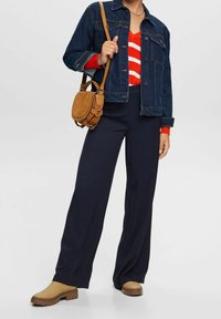 Jeansjacke, rot-weißer gestreifter Pullover, marineblaue weit geschnittene Hose, braune Stiefeletten und eine beigefarbene Umhängetasche. Texturiertes und lässiges Design.