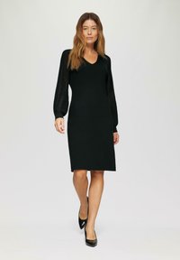 Robe en maille noire avec un décolleté en V et de longues manches bouffantes présentant une texture à côtes verticales. La coupe arrive au genou et est ajustée.
